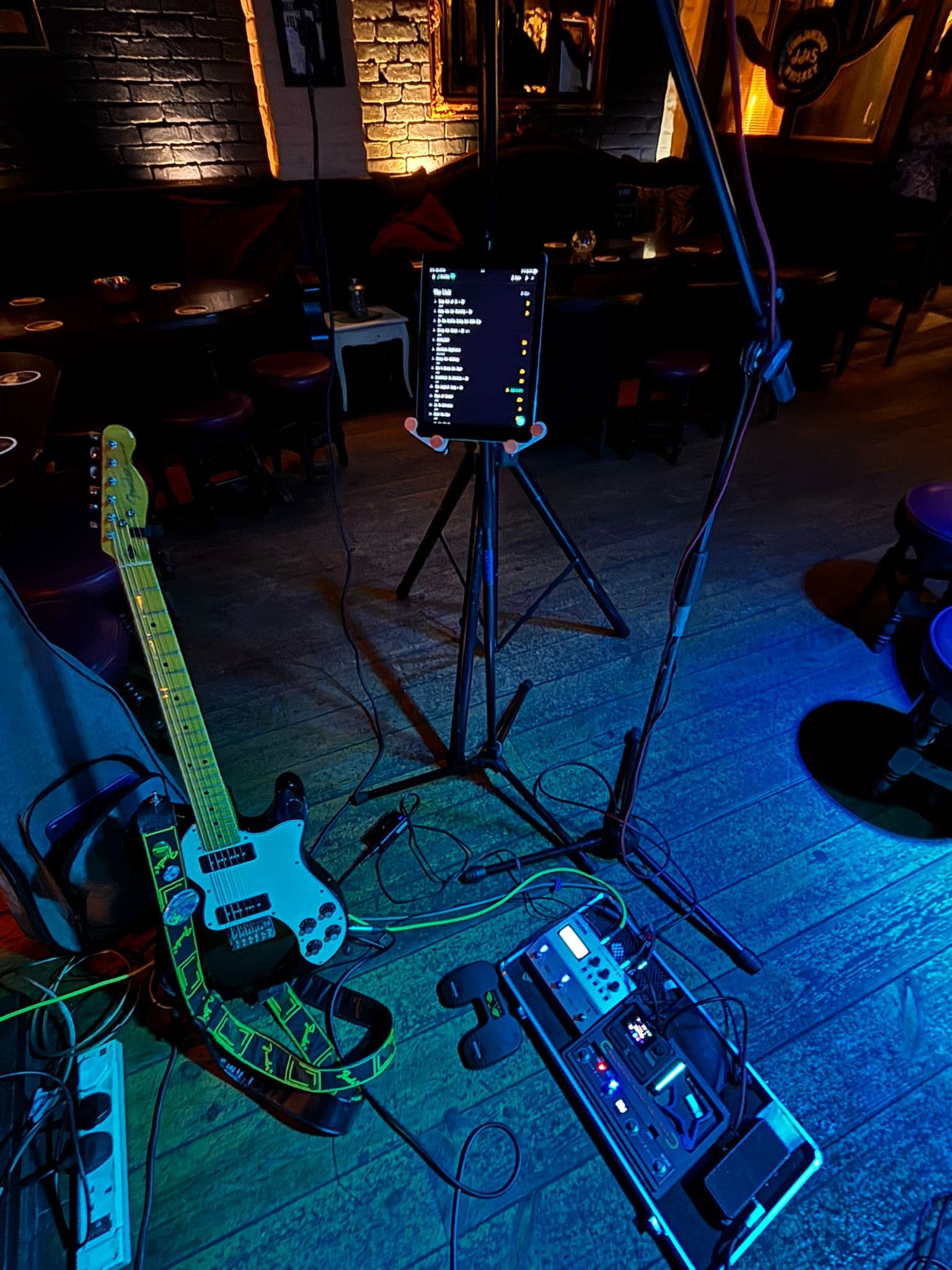 Geoff's tablet on a mic stand at a pub gig in Ireland, running Fretlist Play Mode. Guitar and pedalboard in the foreground.